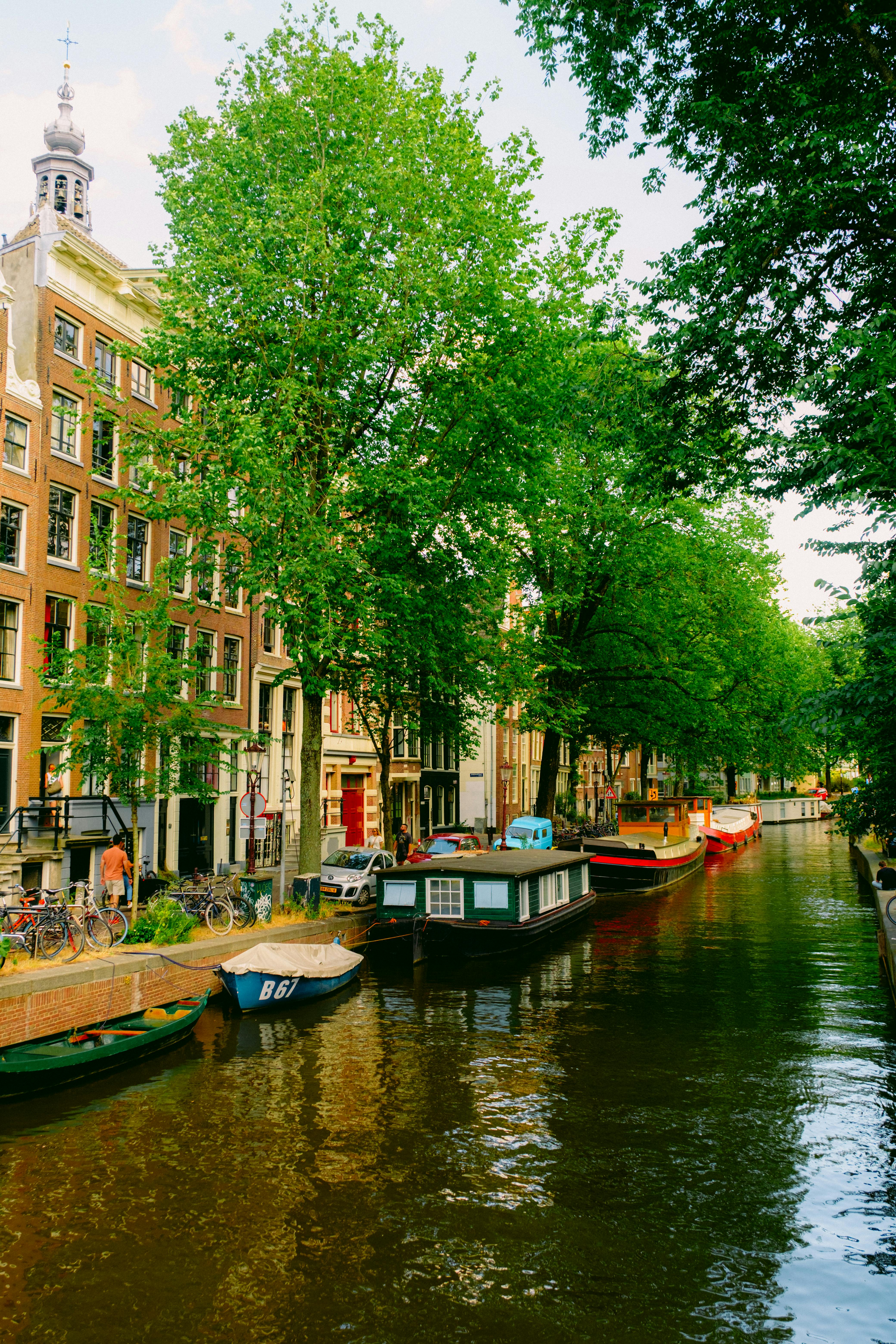 Amsterdam canals with lush green trees in summer, photorealistic, sunny day, iconic Dutch architecture